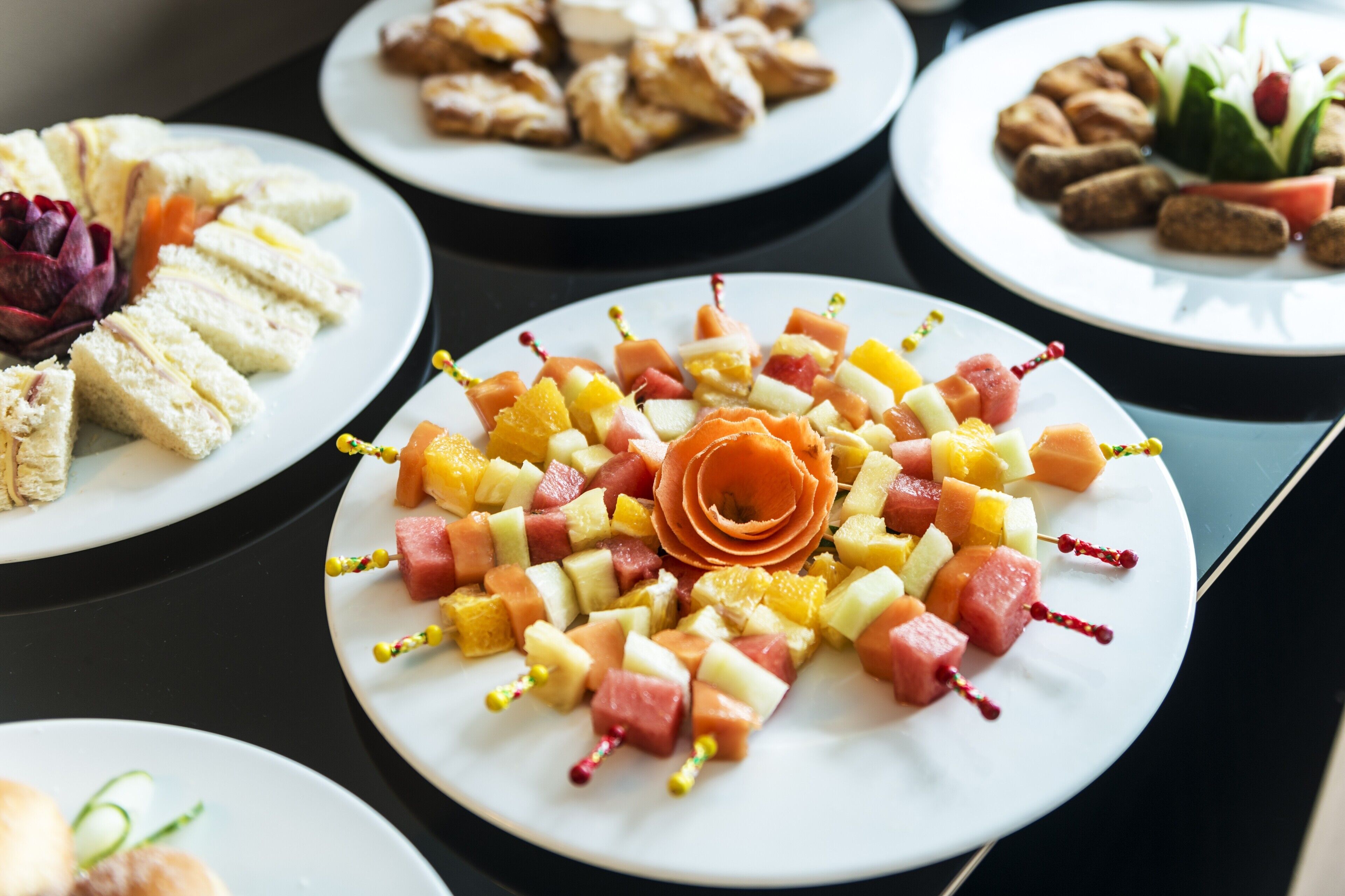 A table with various food items including fruit skewers and sandwiches.