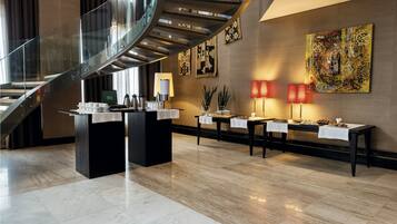 A modern lobby with a glass staircase, marble flooring, and a reception desk with a coffee station.