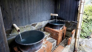 A traditional Japanese onsen with stone and brick structures, two large hot tubs, and a bamboo water spout.