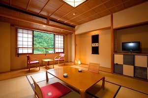 Una habitación japonesa tradicional con suelo de tatami, una mesa baja de madera y un televisor sobre un mueble.