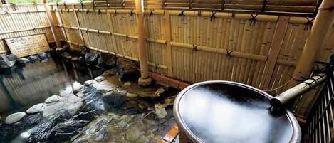 Un onsen japonés tradicional con un baño de piedra, paredes de bambú y un jacuzzi humeante.