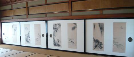 Una habitación japonesa tradicional con suelo de tatami, puertas correderas decoradas con obras de arte y techo de madera.