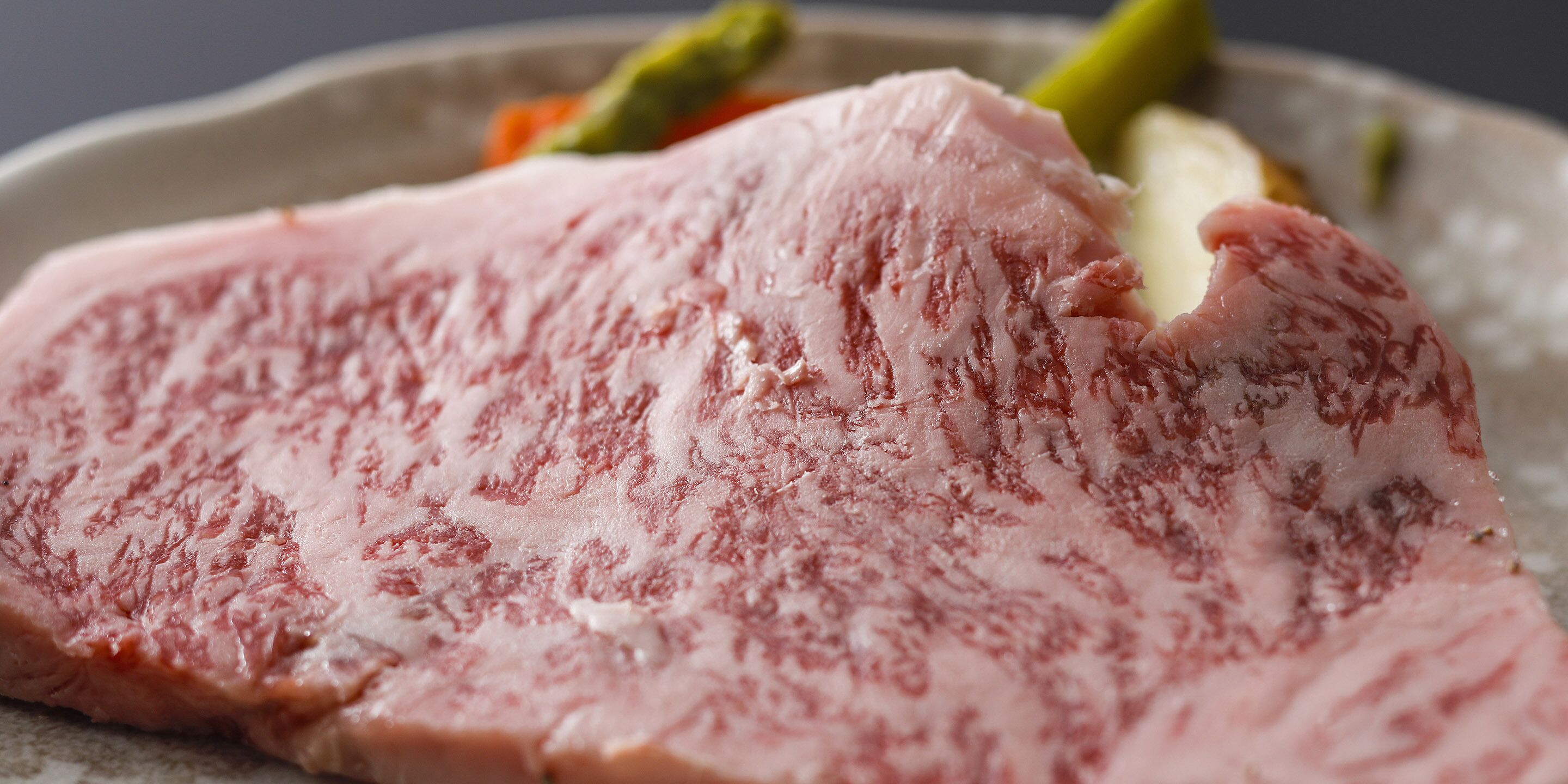 A close-up of a raw pork chop with visible marbling, served on a plate with vegetables.