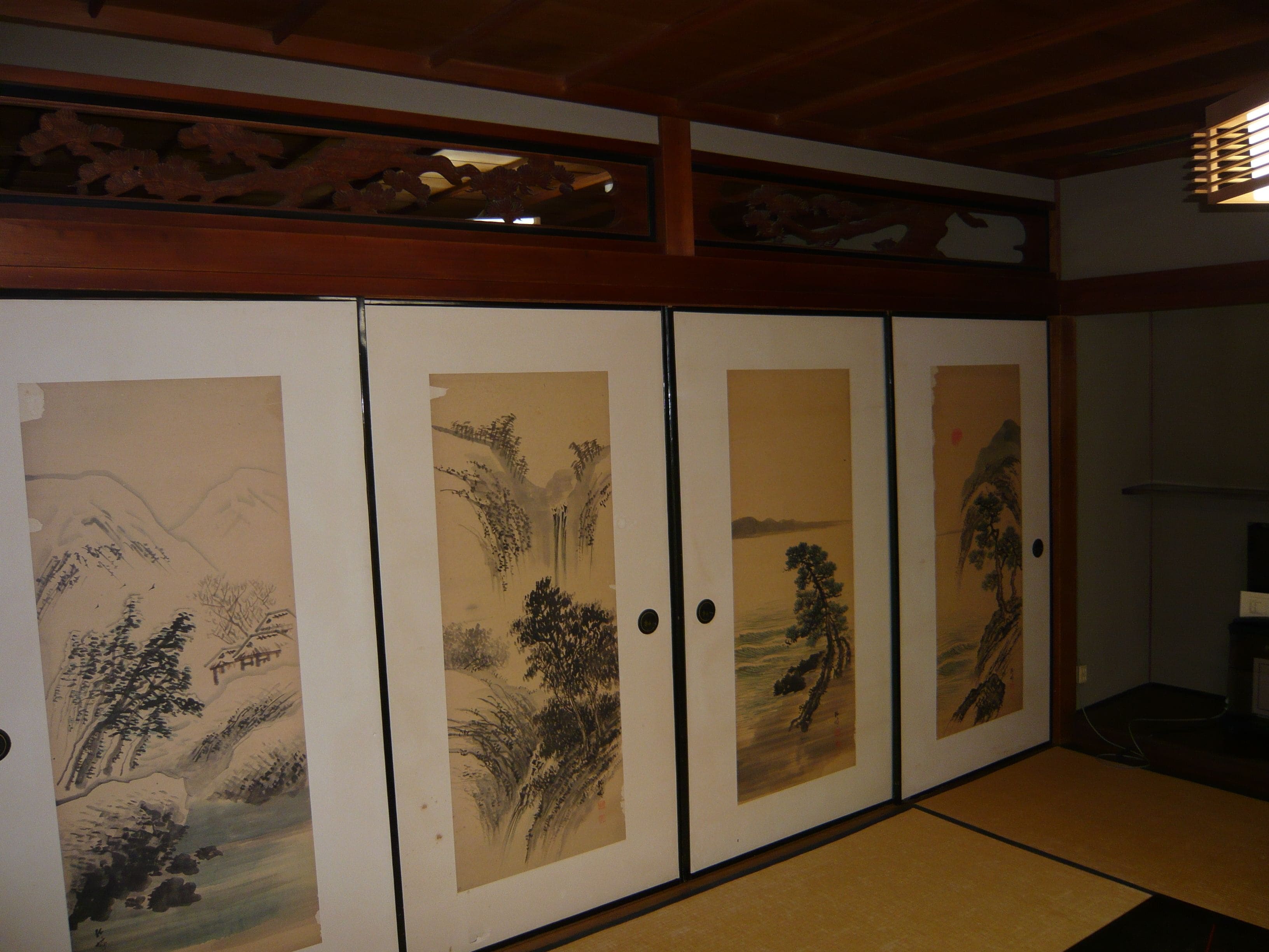 A traditional Japanese room with tatami flooring, shoji screens, and sliding doors with artwork.