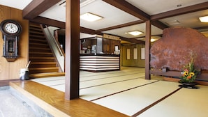 Un interior japonés tradicional con suelo de tatami, un mostrador de recepción, una escalera de madera y una gran escultura de roca.