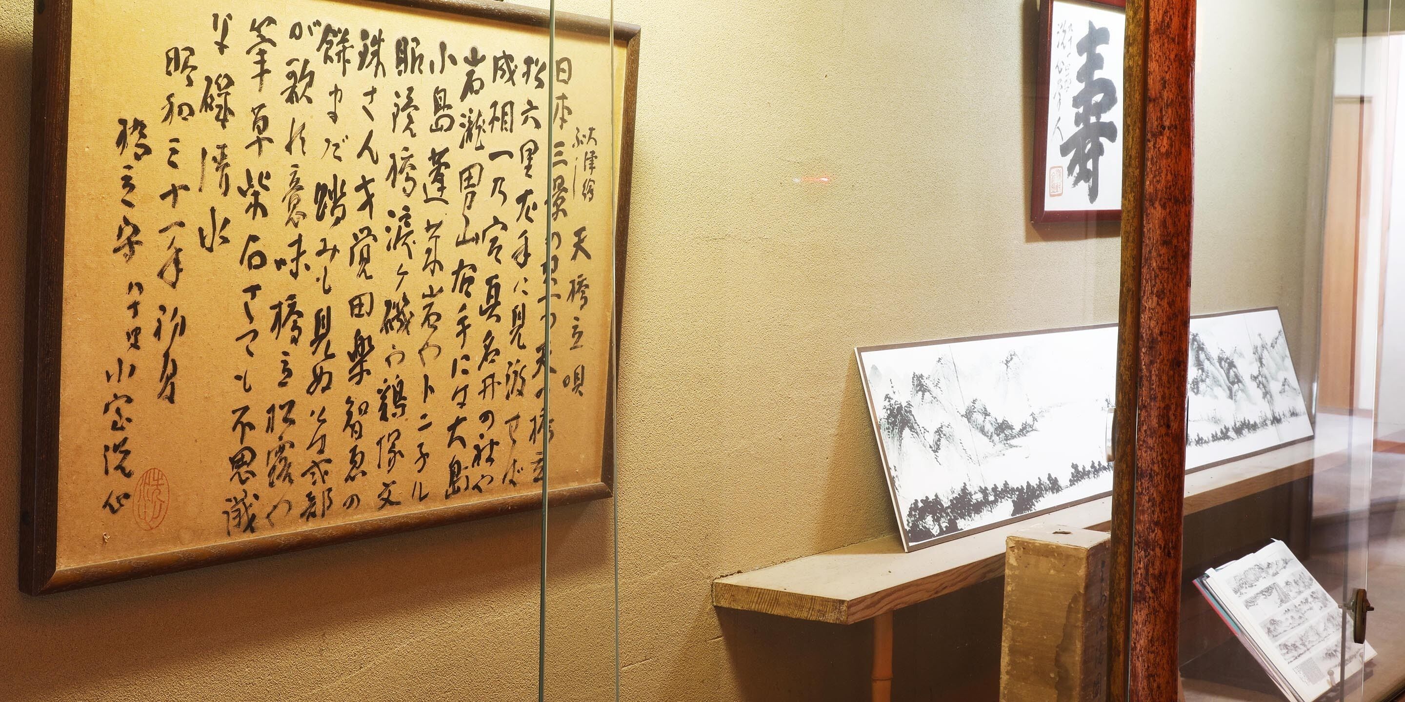 Eine traditionelle japanische Kalligraphie-Wandrolle an einer Wand in einem Zimmer mit Holzboden und Glastrennwand.