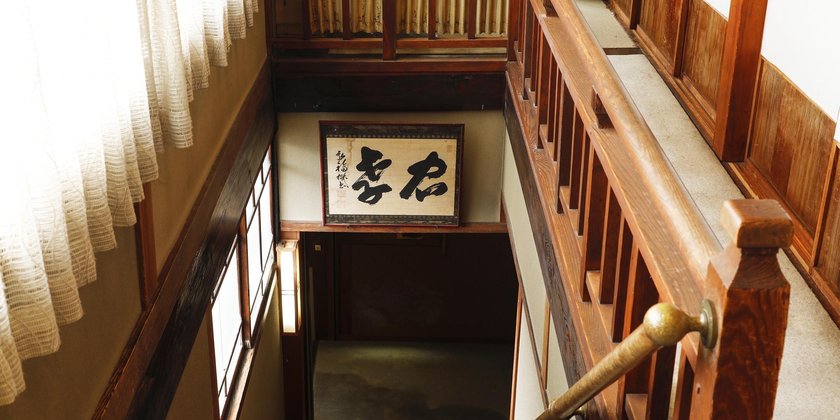 Una escalera de madera tradicional con suelo de esteras de tatami y una obra de caligrafía enmarcada en la pared.