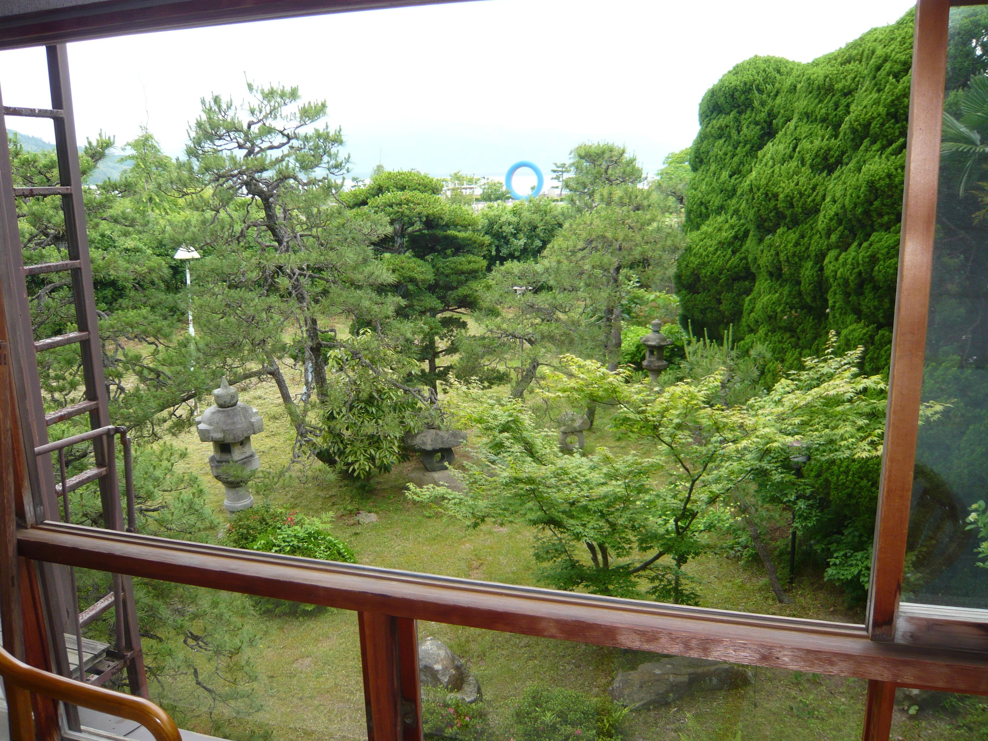 Vista desde una ventana a un jardín con faroles de piedra y árboles.