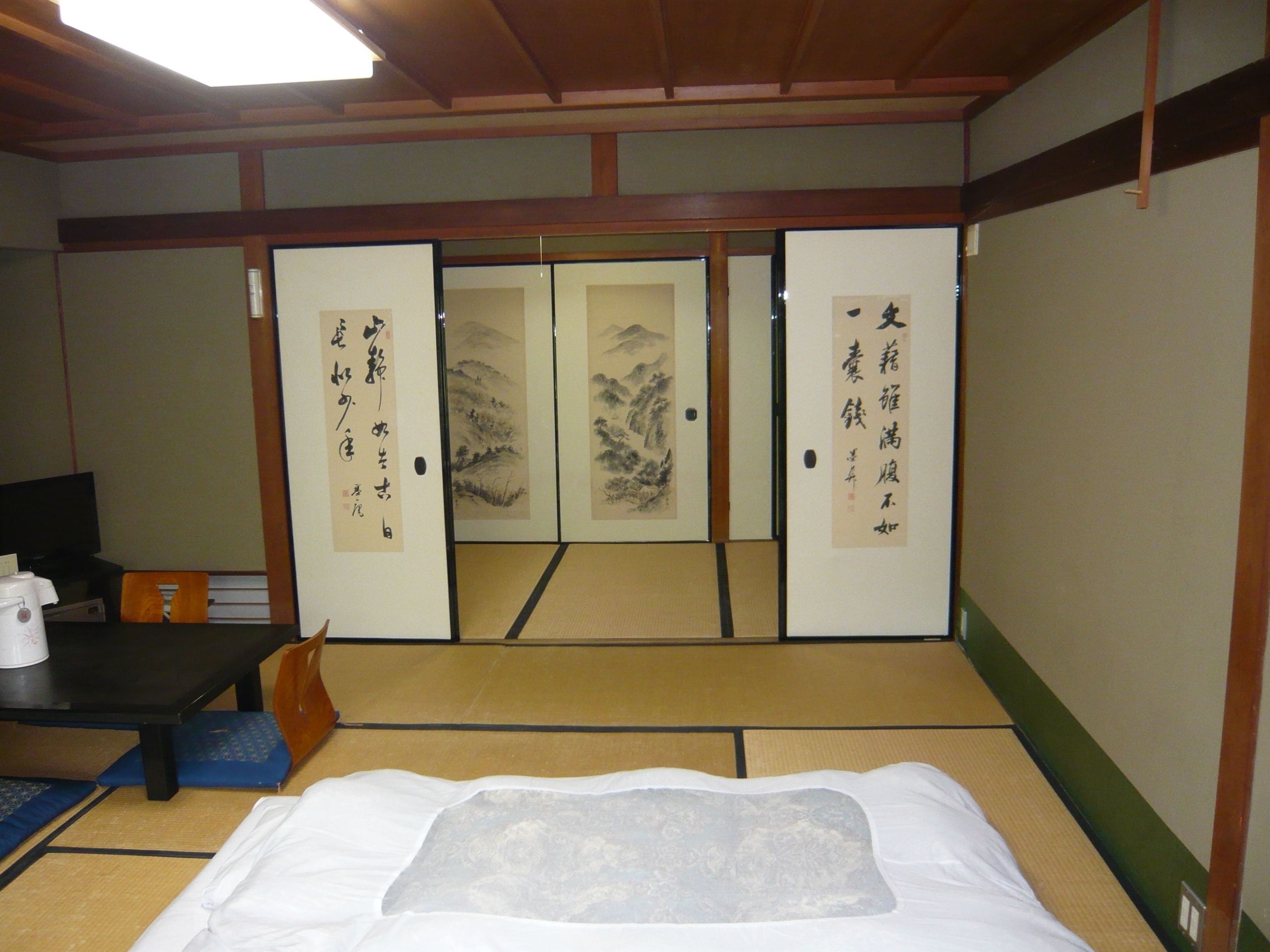 A traditional Japanese room with tatami flooring, a futon bed, a low table with a kettle, and sliding doors with calligraphy.