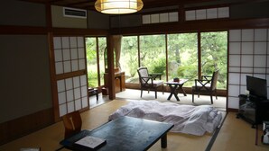 Una habitación japonesa tradicional con suelo de tatami, una mesa baja, sillas y un televisor.