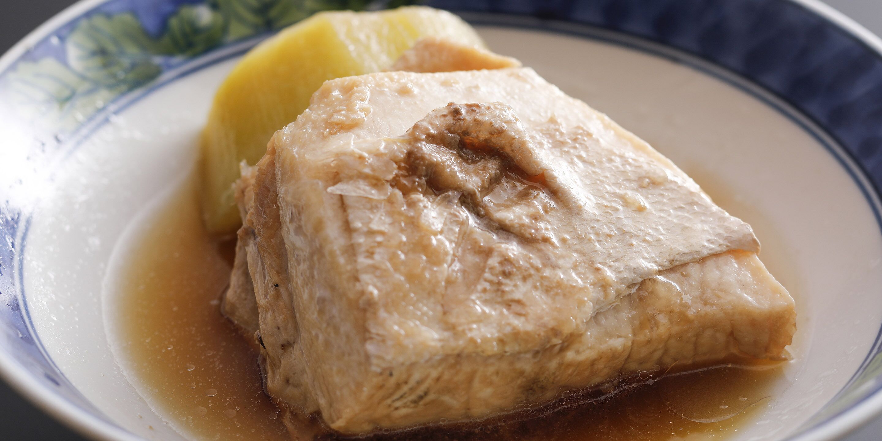 A piece of meat with a sauce, possibly a stew or curry, served on a plate with a decorative rim.