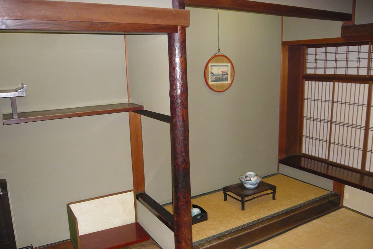 Una habitación japonesa tradicional con suelo de tatami, una mesa de madera baja con un cuenco y un cuadro colgado.