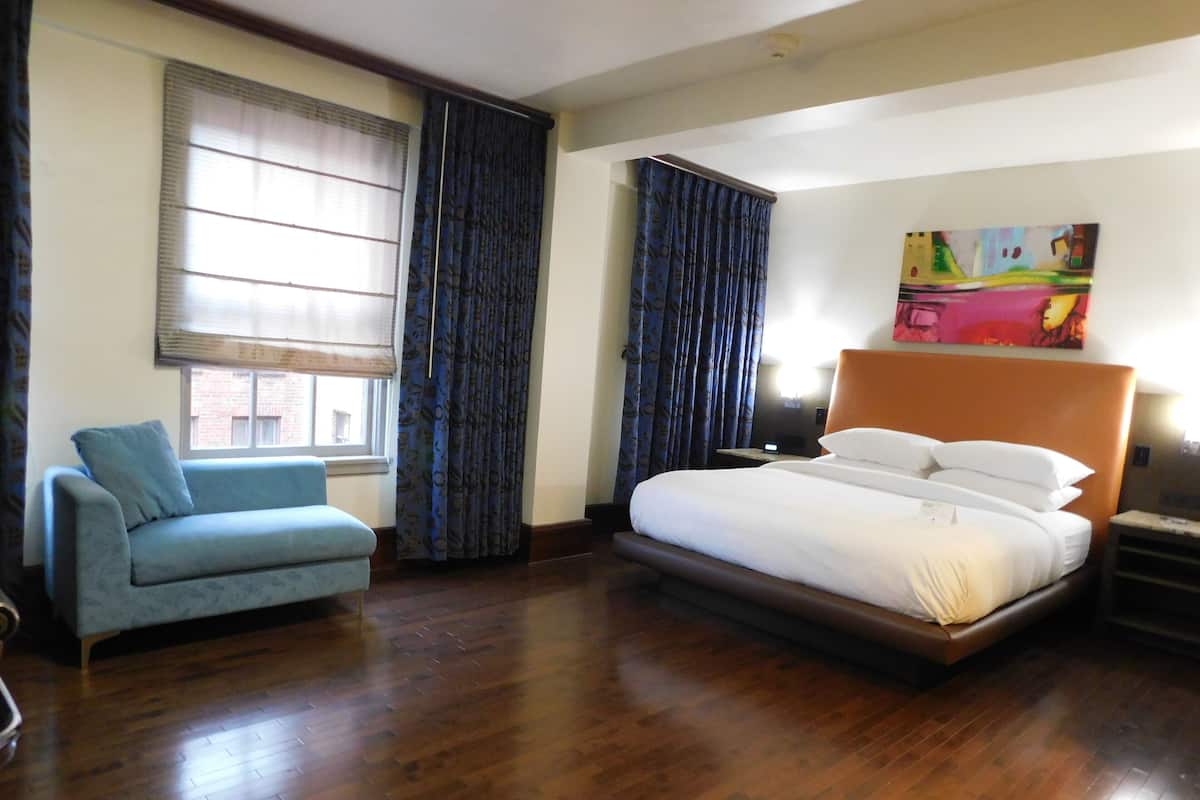 A hotel room with a bed, a blue armchair, and a large window with curtains.