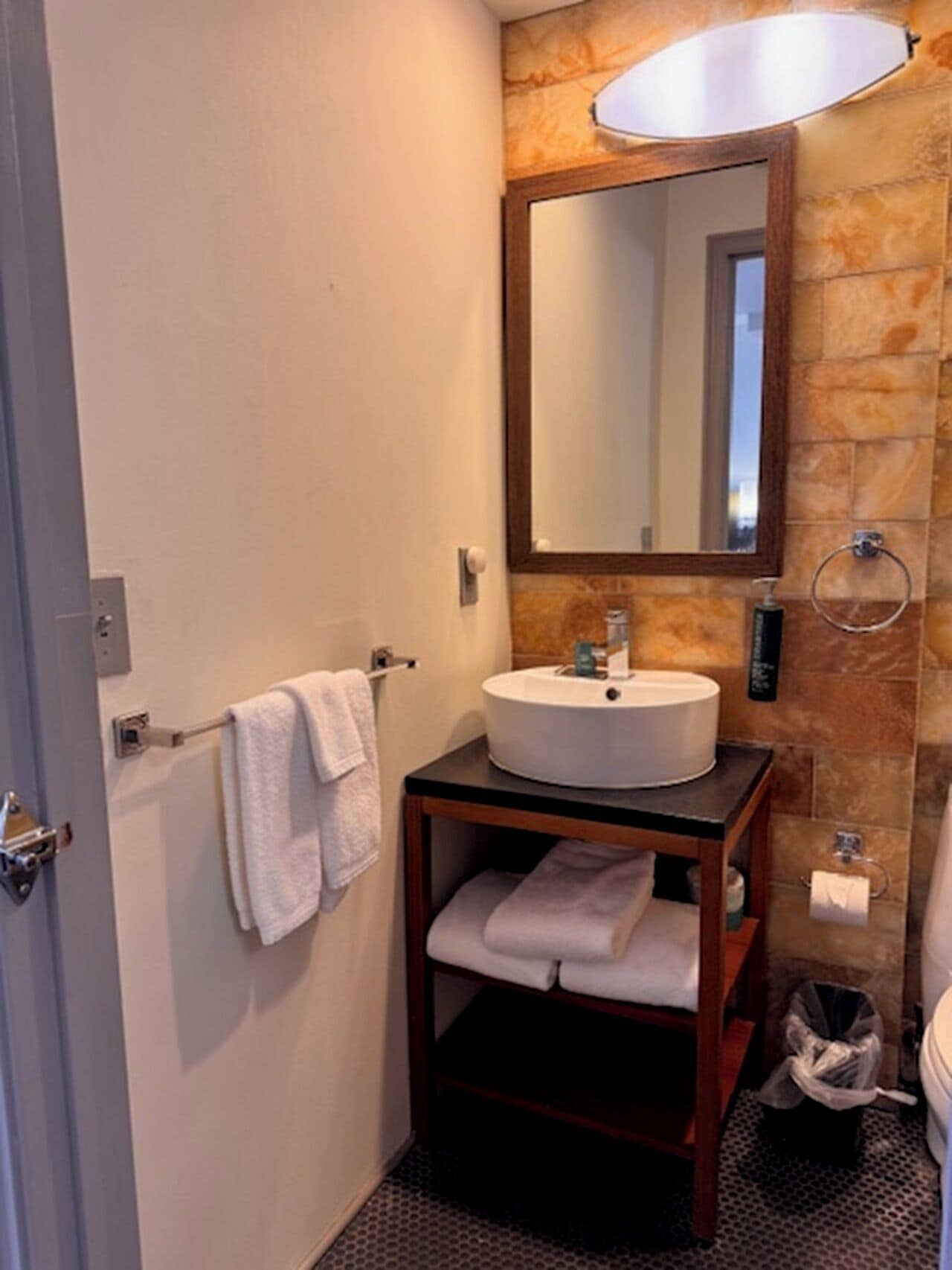 A compact bathroom with a white sink, a mirror, a towel rack, and a trash bin.