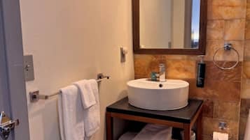 A compact bathroom with a white sink, a mirror, a towel rack, and a trash bin.