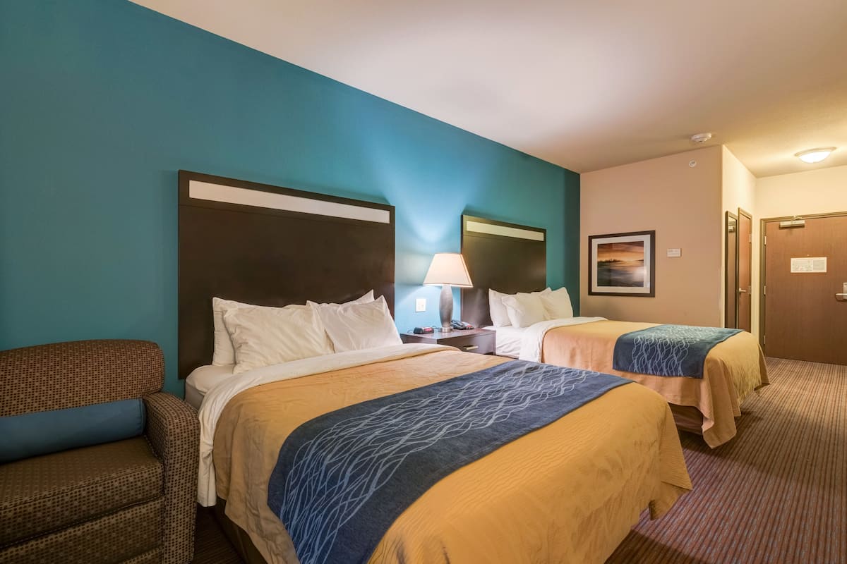 A hotel room with two beds, a nightstand, a lamp, and a framed picture on the wall.