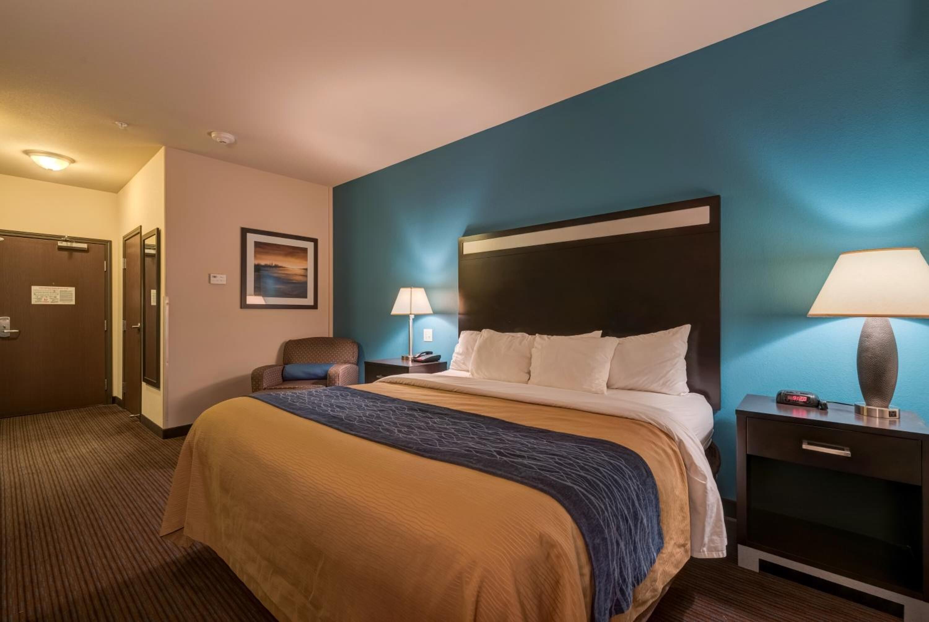 A hotel room with a large bed, two bedside tables, a chair, and a door.