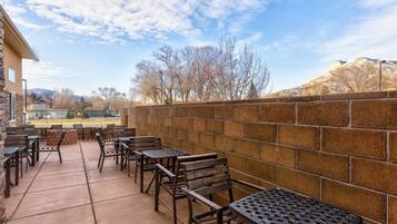 Un patio al aire libre con mesas y sillas, un muro de piedra y una vista de árboles y montañas al fondo.