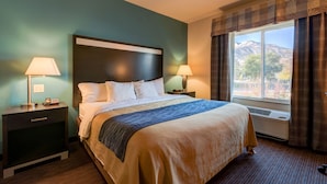 A hotel room with a large bed, two bedside tables with lamps, a window with curtains, and a view of mountains. - Grand Vista Hotel Parachute (Parachute)