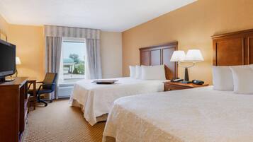 A hotel room with two beds, a desk with a television, a chair, and a window with curtains.