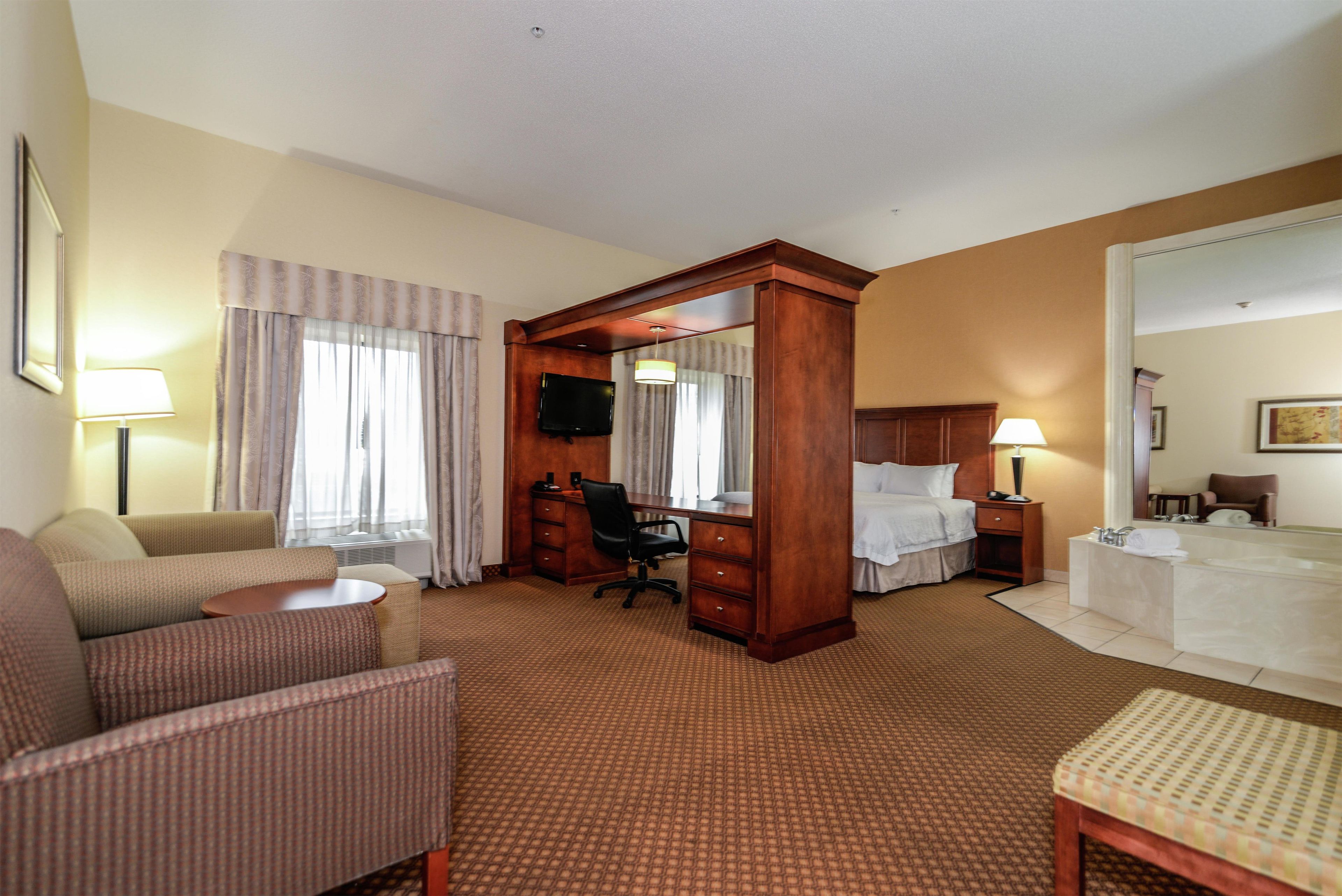 A hotel room with a bed, a desk, a chair, a sofa, a small table, and a bathroom with a sink and mirror.