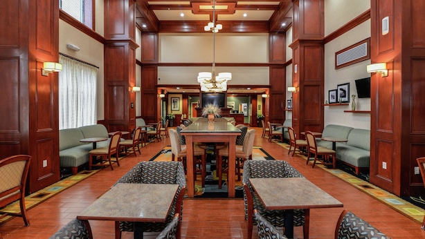 A spacious hotel lobby with a central dining area, multiple seating options including sofas and tables, and a chandelier. - Hampton Inn & Suites Detroit/Chesterfield Township (New Baltimore)