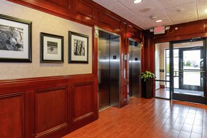A hallway with framed pictures on the wall, an elevator, and a door leading outside.
