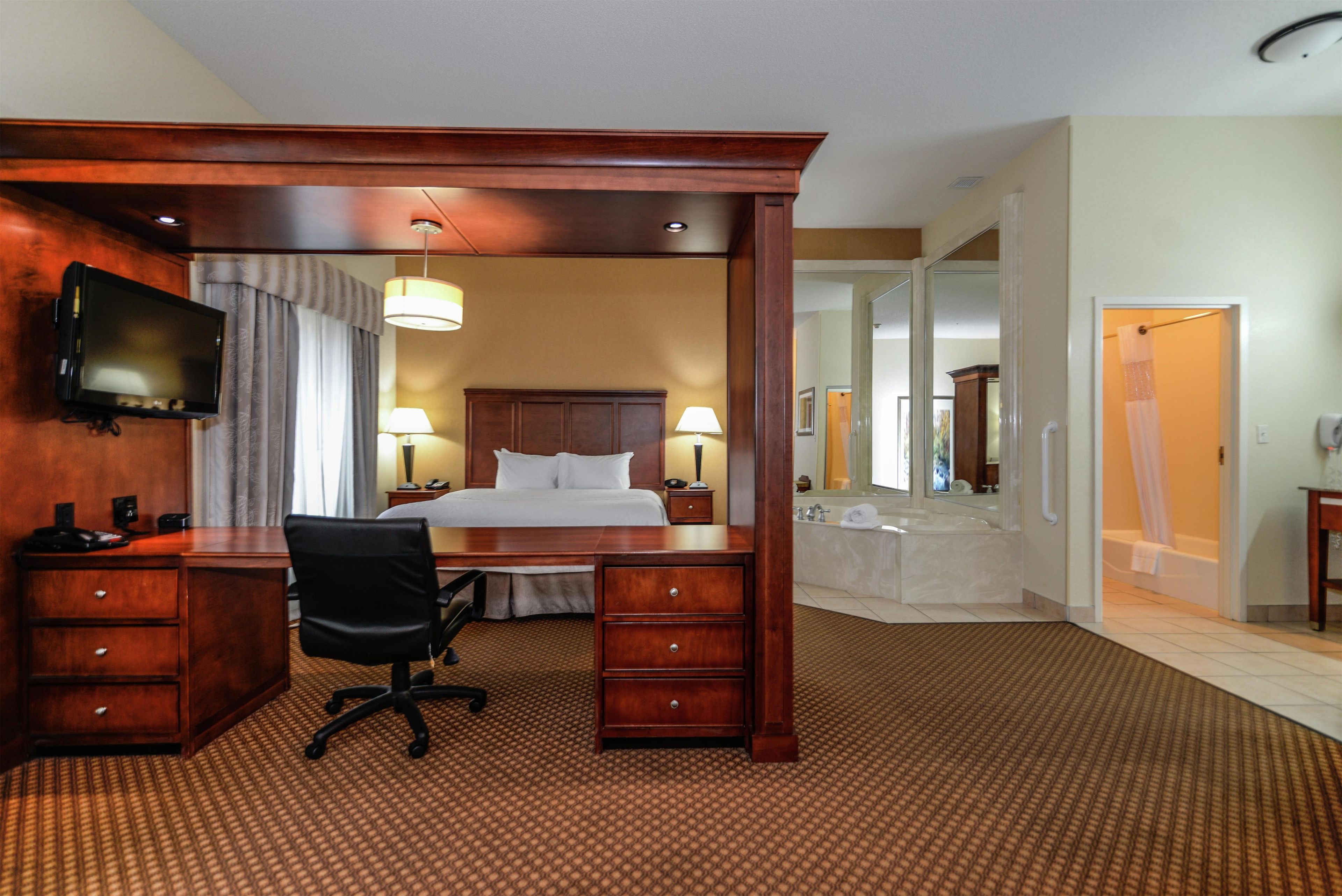 A hotel room with a large bed, a desk with a chair, a television, and a bathroom with a bathtub and shower.