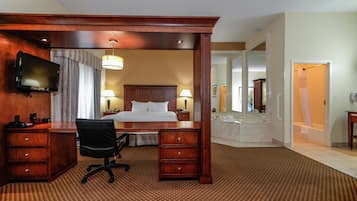 A hotel room with a large bed, a desk with a chair, a television, and a bathroom with a bathtub and shower.