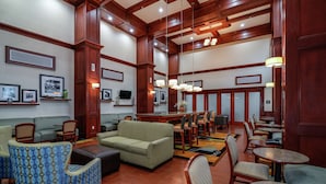 A spacious lobby with a green sofa, patterned armchairs, and a dining area with wooden tables and chairs. - Hampton Inn & Suites Detroit/Chesterfield Township (New Baltimore)