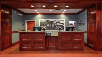 A hotel reception desk with a large framed advertisement, a digital screen, and a sign indicating 'Manager on Duty'.