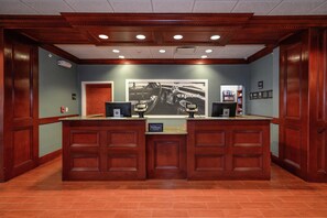 A hotel reception desk with a large framed advertisement, a digital screen, and a sign indicating 'Manager on Duty'.