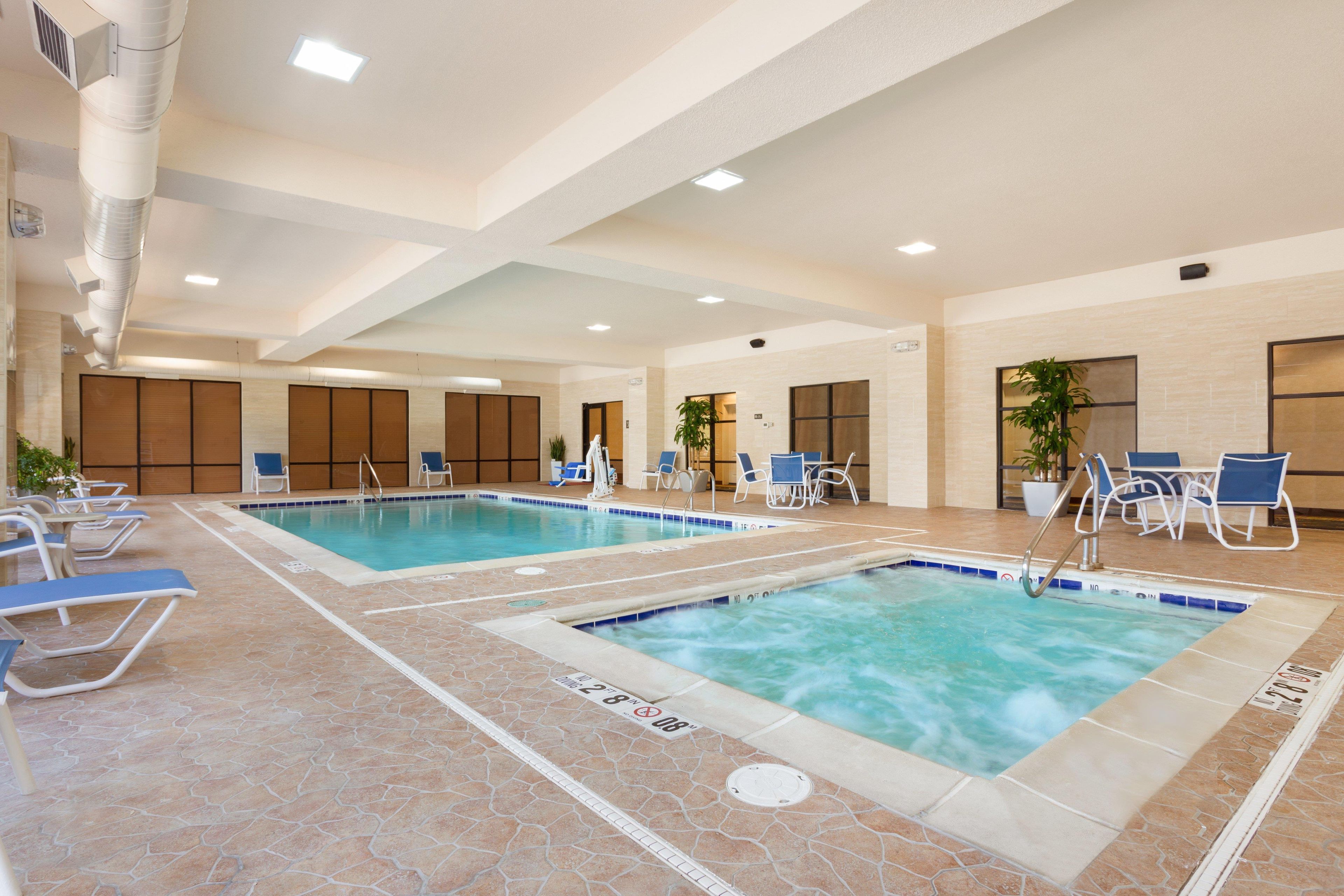 An indoor swimming pool with multiple lanes, lounge chairs, and a seating area with tables.