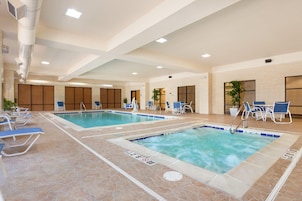 Una piscina interior con varias pistas, sillas de descanso y una zona de estar con mesas.