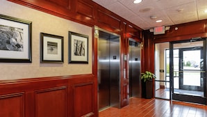 A lobby with framed pictures on the wall, an elevator, and a potted plant. - Hampton Inn & Suites Detroit/Chesterfield Township (New Baltimore)