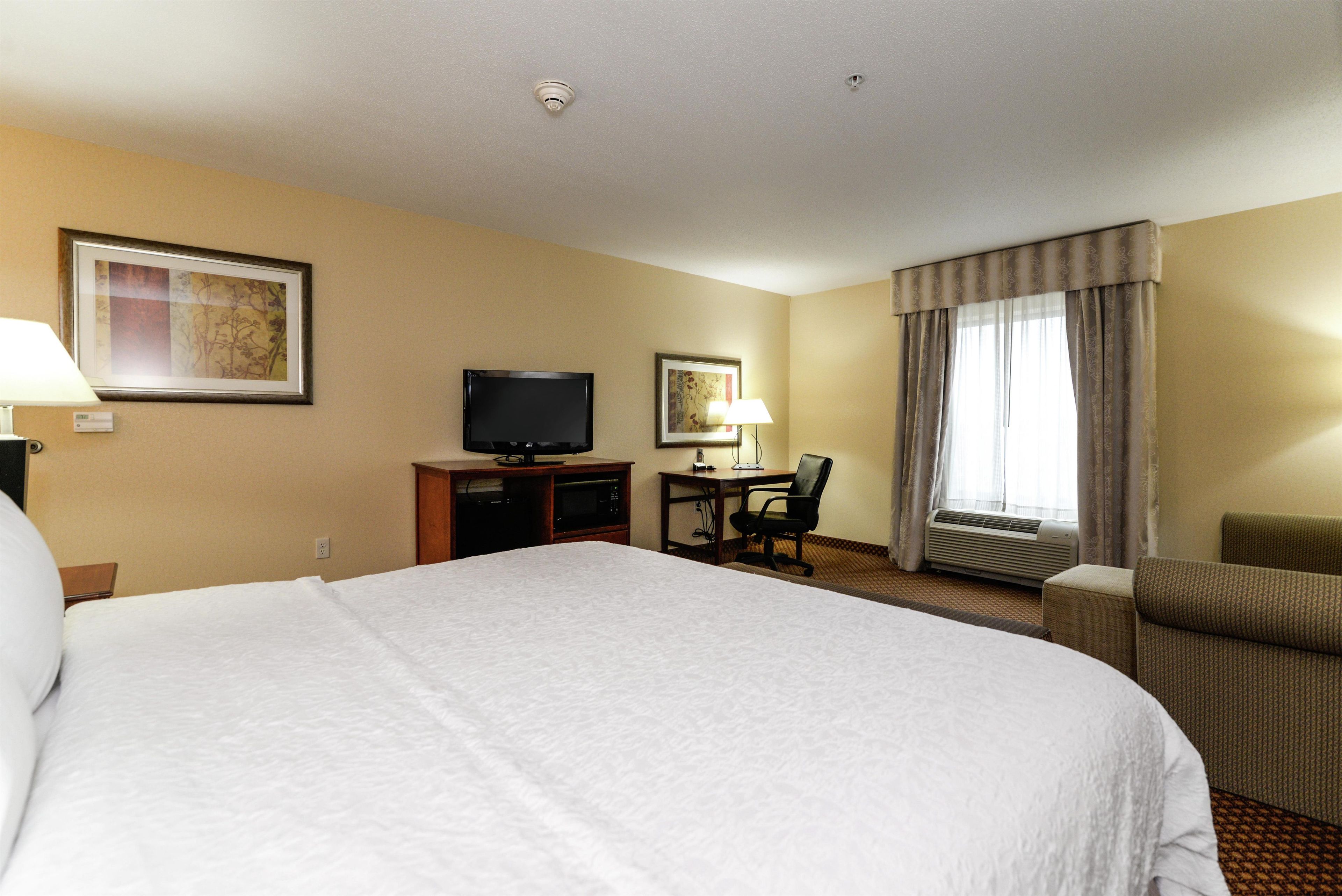 Een hotelkamer met een groot bed, een bureau met een televisie, een stoel en een raam met gordijnen.