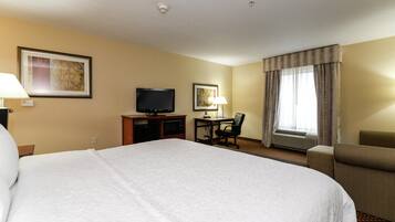 Een hotelkamer met een groot bed, een bureau met een televisie, een stoel en een raam met gordijnen.