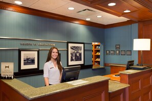 A hotel reception desk with a 'Welcome to Chesterfield' sign, framed pictures on the wall, and a desk with a computer and a lamp.