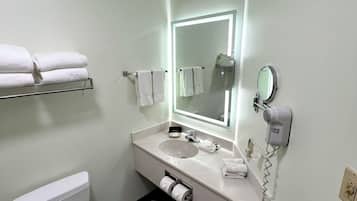 Un baño moderno con inodoro, lavabo y espejo. Hay toallas en un estante y un secador de pelo en la pared.