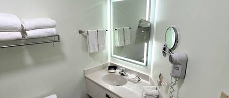 Une salle de bain moderne avec des toilettes, un lavabo et un miroir. Des serviettes sont posées sur une étagÚre et un sÚche-cheveux est fixé au mur.