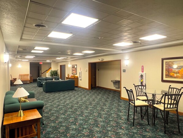 A hotel lobby with a green carpet, a sofa, a table with chairs, and a painting on the wall. - Van Buren Hotel (Shipshewana)