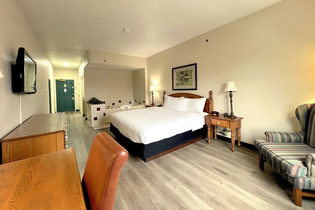 A hotel room with a bed, bedside table, lamp, chair, and a desk.