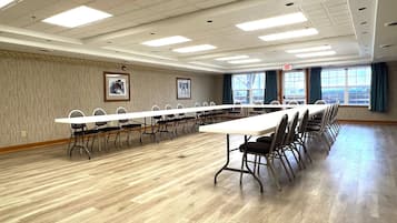 Un salón de conferencias con una larga mesa y sillas, ventanas amplias con cortinas y cuadros en las paredes.