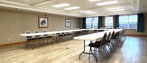 A conference room with a long table and chairs, large windows with curtains, and framed pictures on the walls.