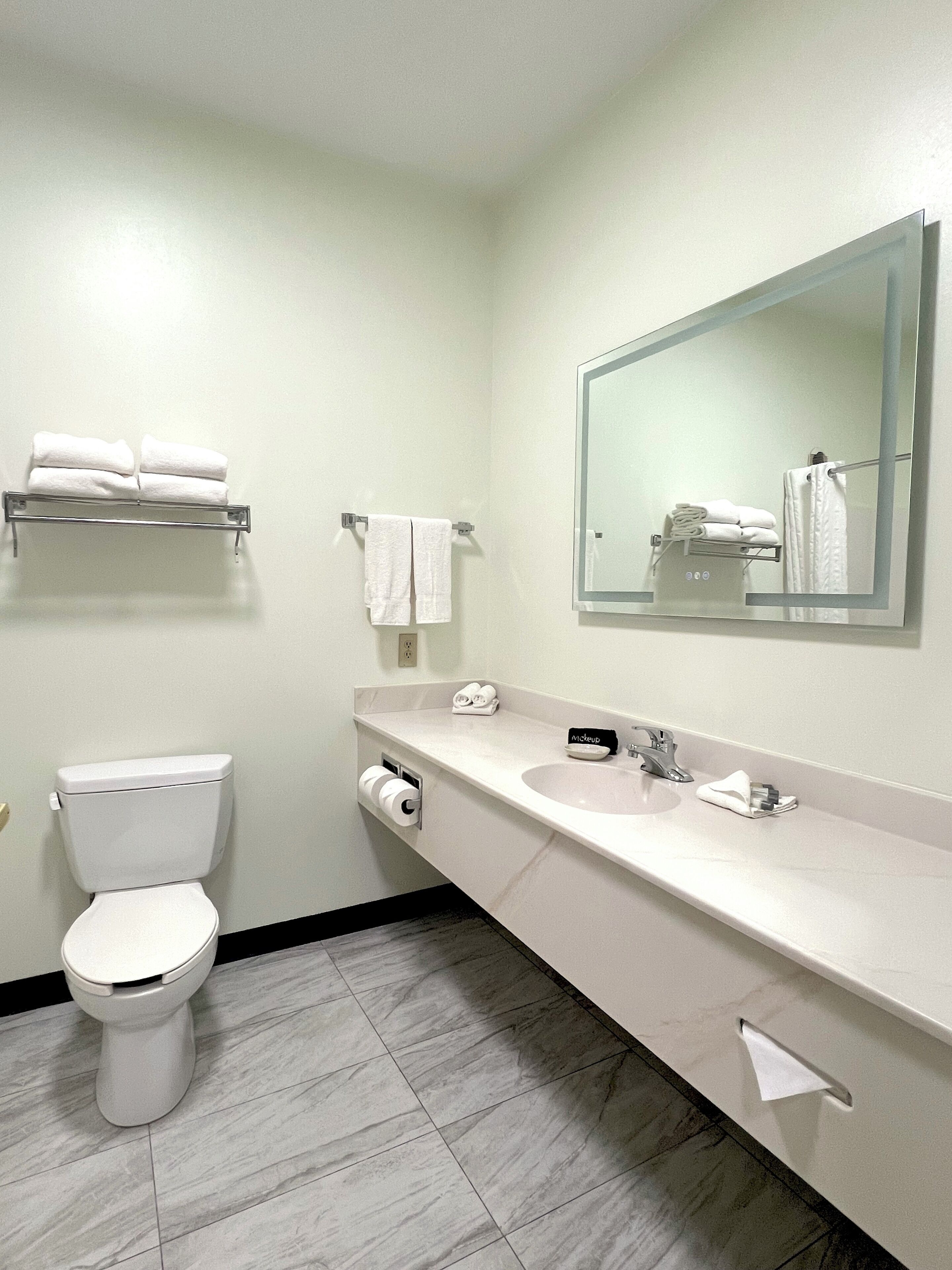 A modern bathroom with a toilet, sink, mirror, towel rack, and a towel dispenser.