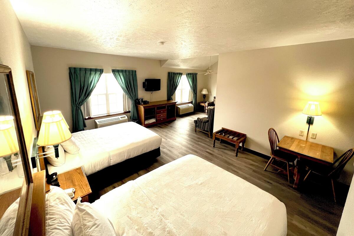 A hotel room with two beds, a desk, a chair, a TV, and a lamp.