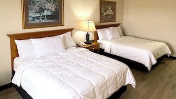 Dos camas individuales con cabeceros de madera, una mesita de noche con lámpara y teléfono, y dos cuadros enmarcados en la pared.