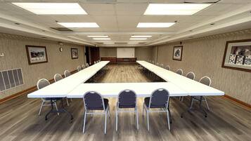 Un salón de conferencias con una larga mesa, sillas y una pantalla para proyector.