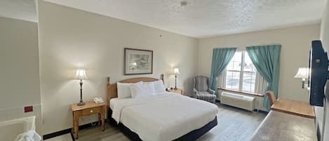 A hotel room with a bed, two bedside tables with lamps, a chair, a desk, a window with curtains, and a framed picture on the wall.