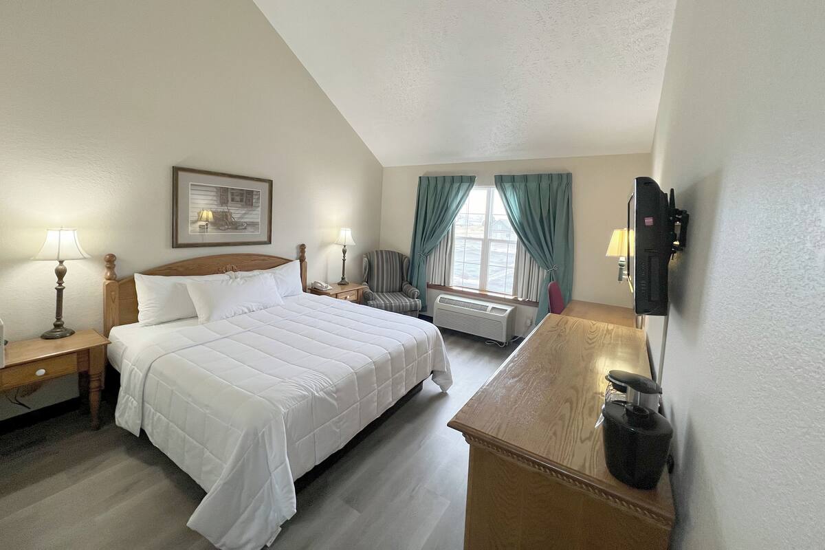 A hotel room with a large bed, a desk, a chair, a TV, and a window with curtains.